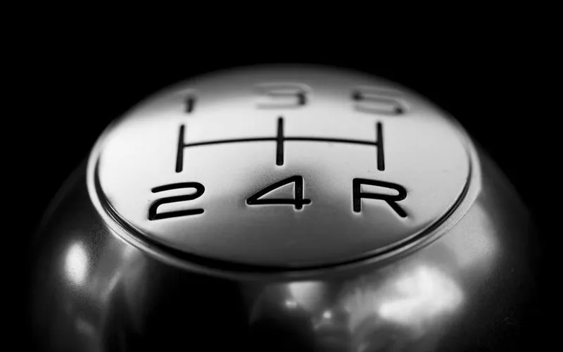 Monochrome close-up of a manual gear stick showing shift positions 1 through R