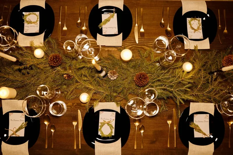 Elegant table setup with pine cones, candles, and dinnerware.”
               title=
